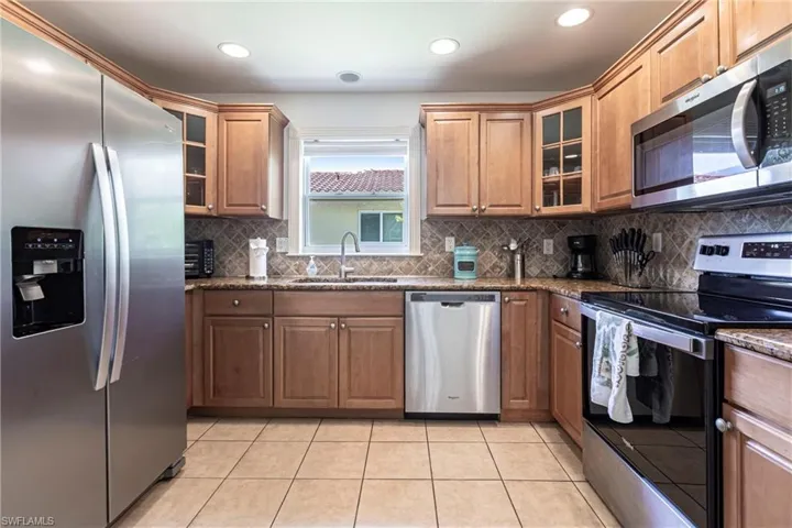 Kitchen with glass fronted cabinets, stainless steel appliances, dark stone counters, wood finish cabinets, and recessed lighting