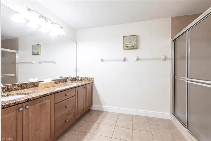 Full bathroom featuring a shower stall, double vanity, and light tile patterned flooring