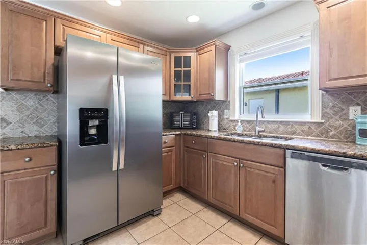 Kitchen featuring stainless steel appliances, dark stone countertops, glass insert cabinets, wood finish cabinetry, and recessed lighting
