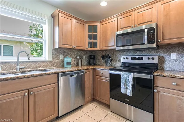Kitchen with stainless steel appliances, glass fronted cabinets, dark stone countertops, and wood finish cabinets
