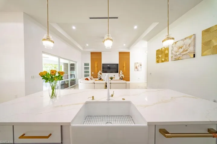 Expansive kitchen island featuring a farmhouse sink, gold-toned hardware, and three pendant light fixtures