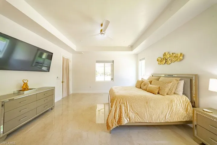 Spacious bedroom featuring light-toned tile flooring, tray ceiling, and a modern ceiling fan