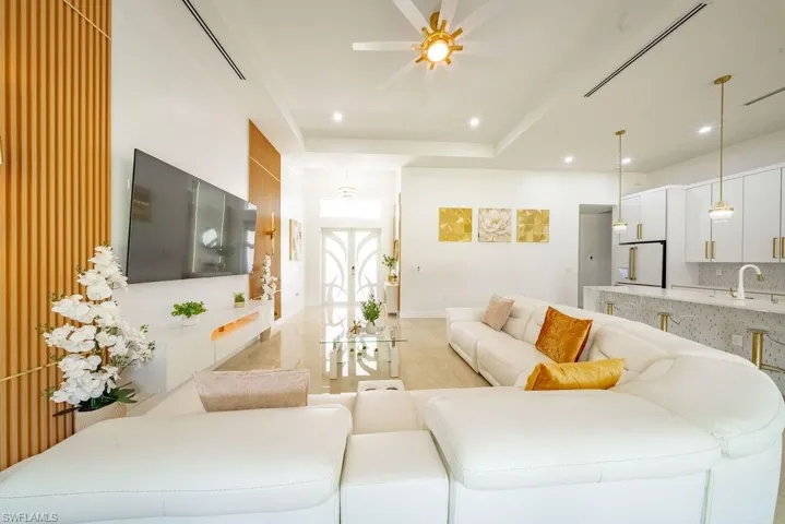 Open-concept living area featuring a modern kitchen with a waterfall island, white cabinetry, and gold-tone hardware