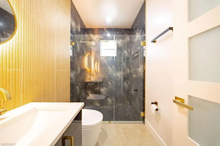 Sleek bathroom featuring a glass-enclosed shower with dark patterned wall tile and gold-finish fixtures