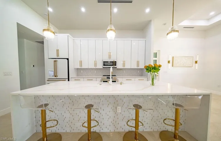 Spacious kitchen featuring an expansive island with a waterfall countertop, white flat-panel cabinetry, a herringbone tile backsplash, and recessed lighting