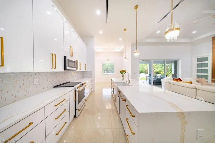 Modern kitchen featuring white high-gloss cabinetry with gold-tone hardware, a waterfall-edge island, and an integrated cooktop