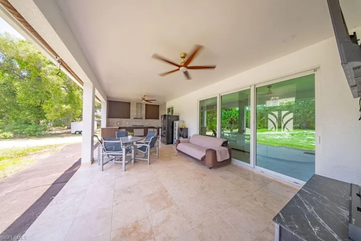 Expansive covered patio featuring a tiled floor, outdoor kitchen with built-in cabinetry, and multiple ceiling fans