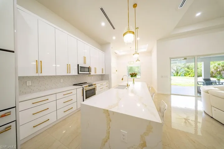 Modern kitchen featuring a waterfall island with stone countertop, white cabinetry with gold-tone hardware, and stainless steel appliances