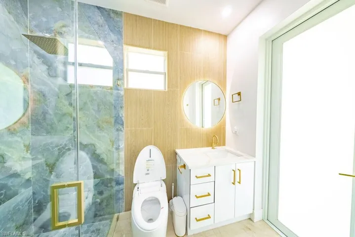 Bathroom featuring a rain shower with a glass enclosure, a wall-mounted vanity with a white countertop, a circular illuminated mirror, and gold-finish fixtures throughout