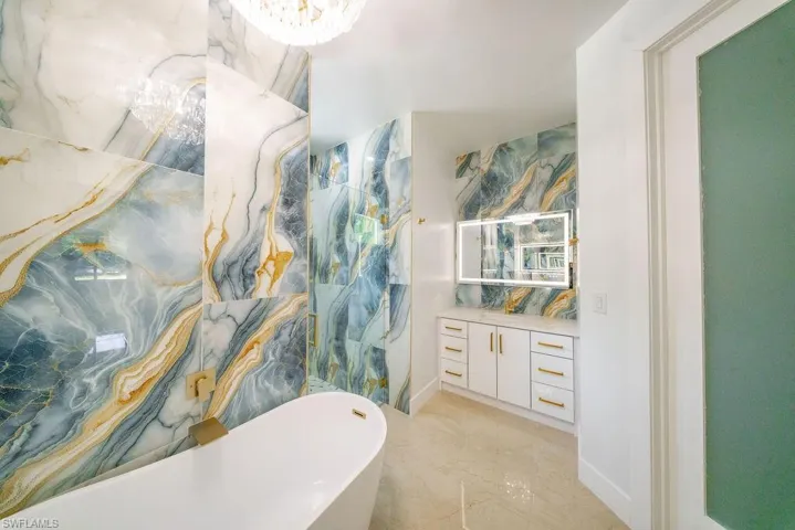 Freestanding soaking tub with gold-tone fixtures against a backdrop of large-format blue and gold veined wall tiles