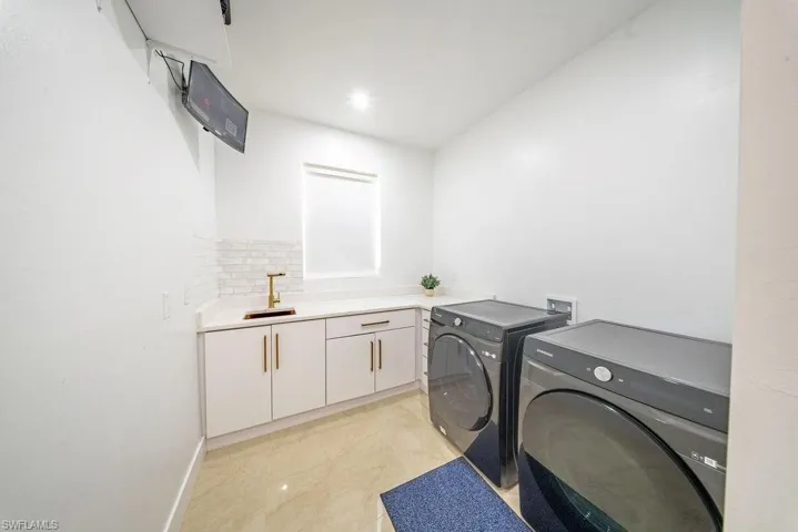 Dedicated laundry space featuring a built-in sink with a gold-finish faucet, white cabinetry with gold-finish hardware, a light-toned countertop, and a white subway tile backsplash
