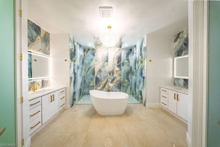 Spacious bathroom featuring a freestanding soaking tub, a walk-in shower with glass enclosure, dual vanity stations with illuminated mirrors, and expansive tile flooring