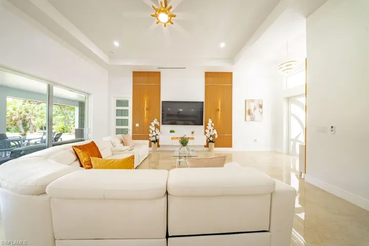 Spacious living area featuring polished tile flooring, a tiered ceiling with recessed lighting, and a modern ceiling fan