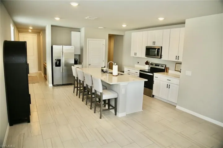 Kitchen with stainless steel appliances, a breakfast bar, white cabinets, an island with sink, and recessed lighting