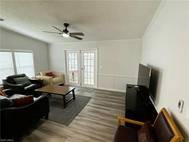 Living room featuring a ceiling fan, a decorative wall, light wood-style floors, french doors, and crown molding
