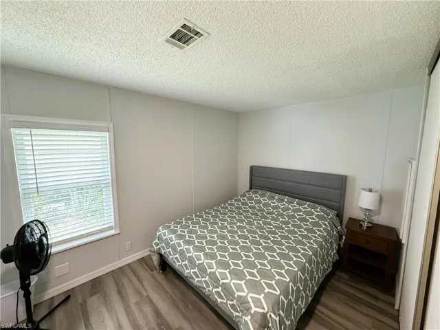 Bedroom with wood finished floors, a textured ceiling, and a decorative wall