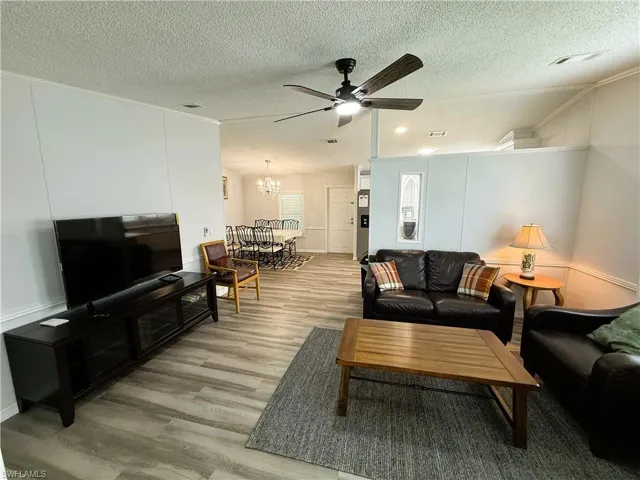 Living area featuring crown molding, a ceiling fan, light wood finished floors, suspended lighting, and a decorative wall