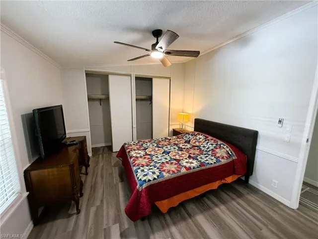Bedroom with wood finished floors, ceiling fan, two closets, and ornamental molding