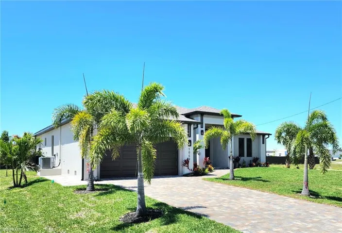 View of front of property featuring a garage, stucco siding, a front lawn, and decorative driveway
