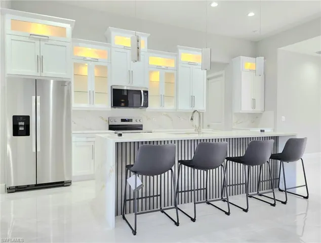 Kitchen featuring a breakfast bar, appliances with stainless steel finishes, a kitchen island with sink, a sink, and decorative backsplash