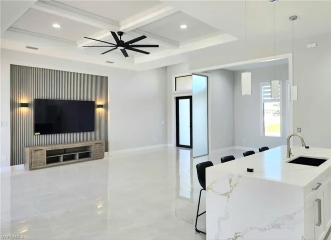 Kitchen featuring coffered ceiling, open floor plan, a sink, and light stone countertops
