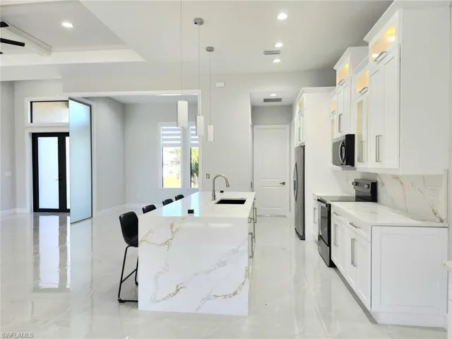 Kitchen with glass insert cabinets, a kitchen bar, recessed lighting, appliances with stainless steel finishes, and a sink
