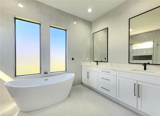 Bathroom with a soaking tub, marble finish floor, a sink, tile walls, and double vanity