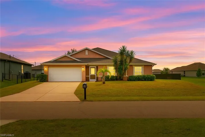 View of front facade with stucco siding, a lawn, driveway, and an attached garage