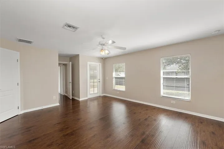 Empty room with dark wood-style floors, healthy amount of natural light, and a ceiling fan