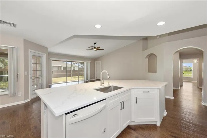Kitchen with white cabinetry, white dishwasher, an island with sink, light stone counters, and dark wood-type flooring