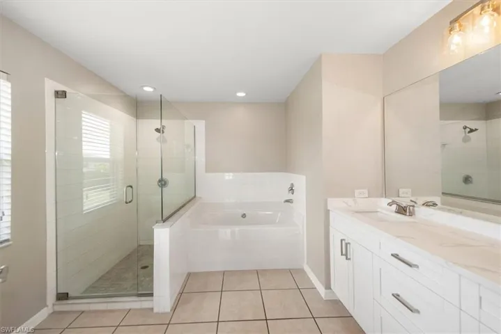 Full bath with light tile patterned floors, double vanity, a bath, a stall shower, and recessed lighting