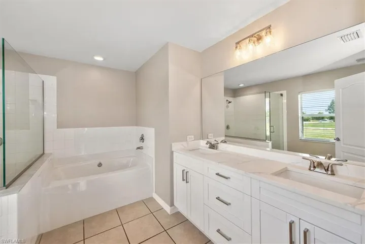 Full bathroom featuring a garden tub, light tile patterned floors, double vanity, and a shower stall