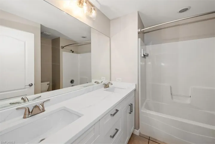 Full bath featuring  shower combination, double vanity, and light tile patterned floors