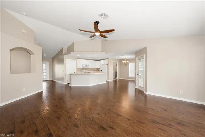 Unfurnished living room featuring dark wood-style flooring, vaulted ceiling, a chandelier, and ceiling fan