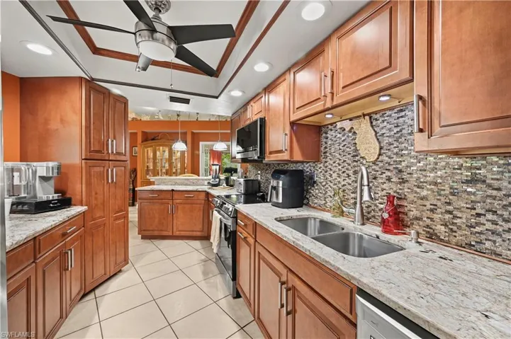 Kitchen featuring hanging light fixtures, light stone counters, stainless steel appliances, ceiling fan, and sink