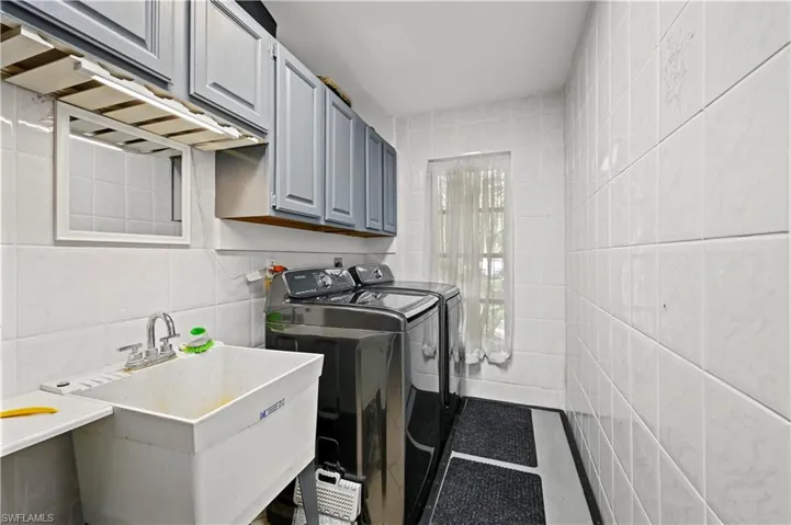 Clothes washing area featuring tile walls, sink, independent washer and dryer, and cabinets