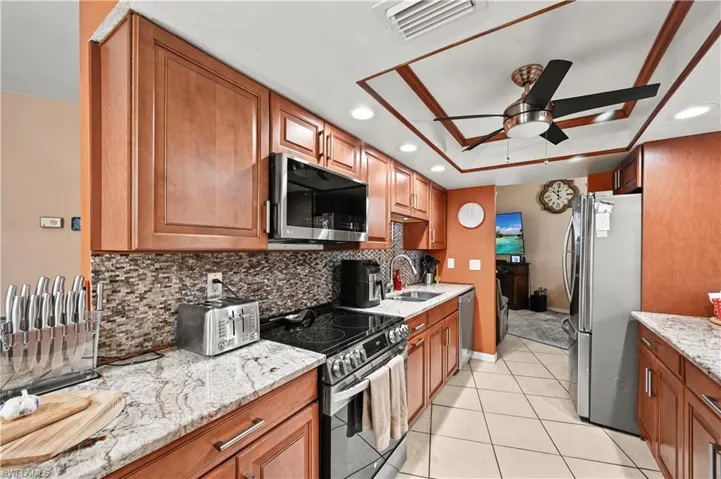 Kitchen with light stone countertops, light tile patterned floors, stainless steel appliances, ceiling fan, and sink
