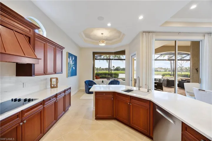 Kitchen with a tray ceiling, stainless steel dishwasher, custom range hood, light stone counters, and hanging light fixtures