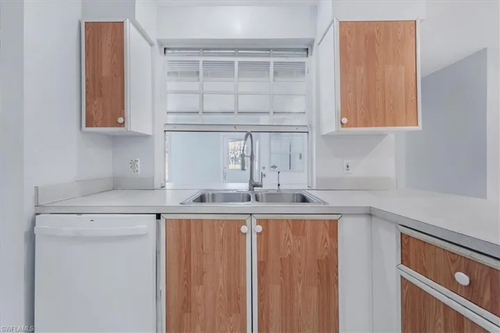 Kitchen with white dishwasher, light countertops, brown cabinets, and white cabinets