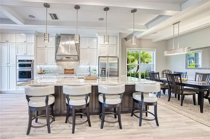 Kitchen with hanging light fixtures, dark brown cabinetry, light wood finished floors, light stone counters, and dishwasher