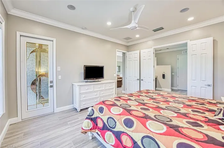 Bedroom with light carpet, crown molding, ceiling fan, and ensuite bath
