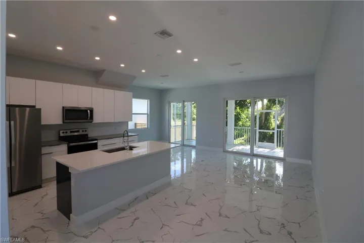 Kitchen featuring a center island with sink, appliances with stainless steel finishes, sink, white cabinetry, and plenty of natural light