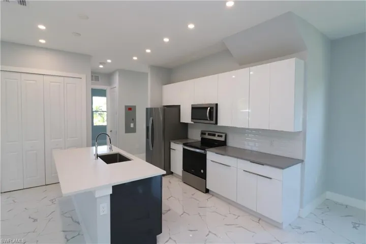 Kitchen featuring appliances with stainless steel finishes, electric panel, white cabinetry, sink, and a kitchen island with sink