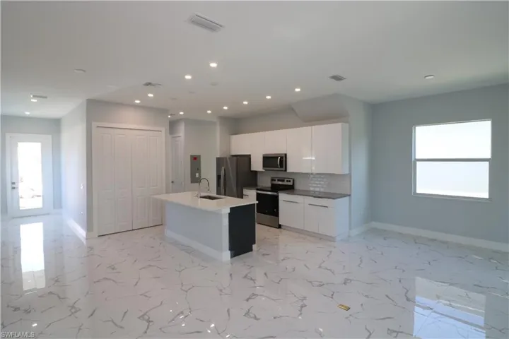 Kitchen with a center island with sink, appliances with stainless steel finishes, sink, decorative backsplash, and white cabinets