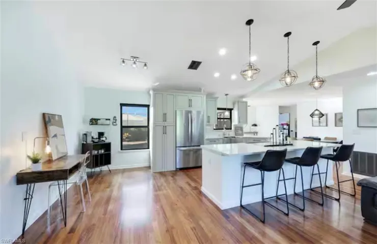 Kitchen featuring a large island, freestanding refrigerator, a breakfast bar area, dark wood finished floors, and pendant lighting