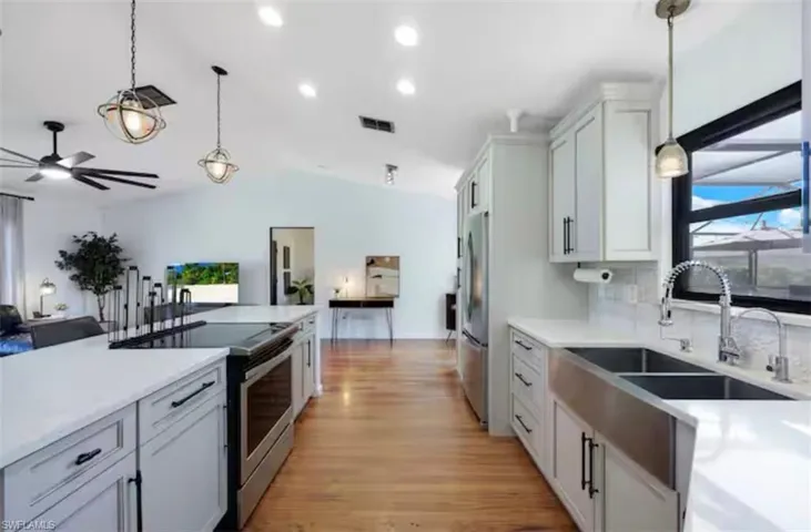 Kitchen with pendant lighting, stainless steel appliances, vaulted ceiling, light wood-style flooring, and light stone counters