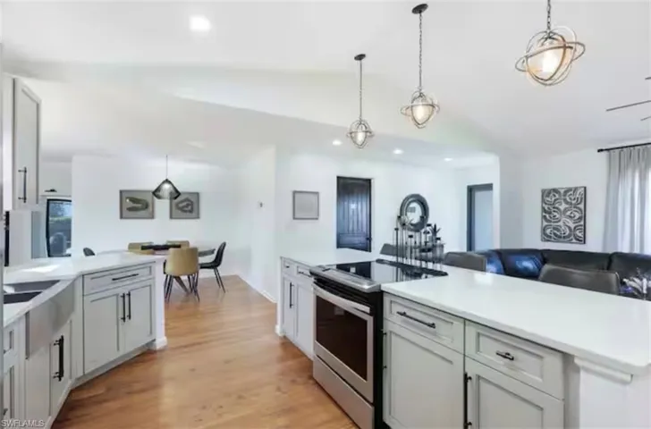Kitchen with stainless steel electric range oven, hanging light fixtures, light wood finished floors, lofted ceiling, and open floor plan