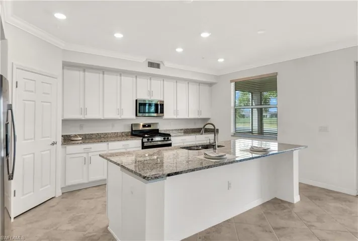Kitchen with appliances with stainless steel finishes, an island with sink, stone counters, sink, and light tile flooring