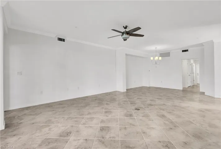 Empty room featuring ceiling fan with notable chandelier, light tile floors, and ornamental molding