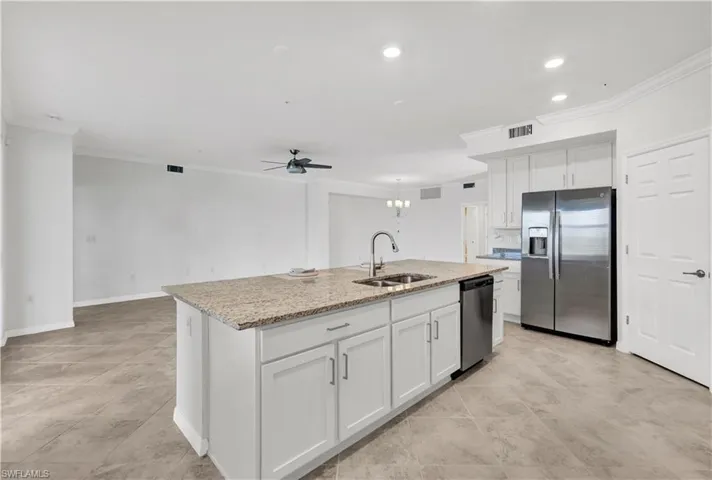 Kitchen featuring ceiling fan with notable chandelier, appliances with stainless steel finishes, white cabinets, a kitchen island with sink, and sink